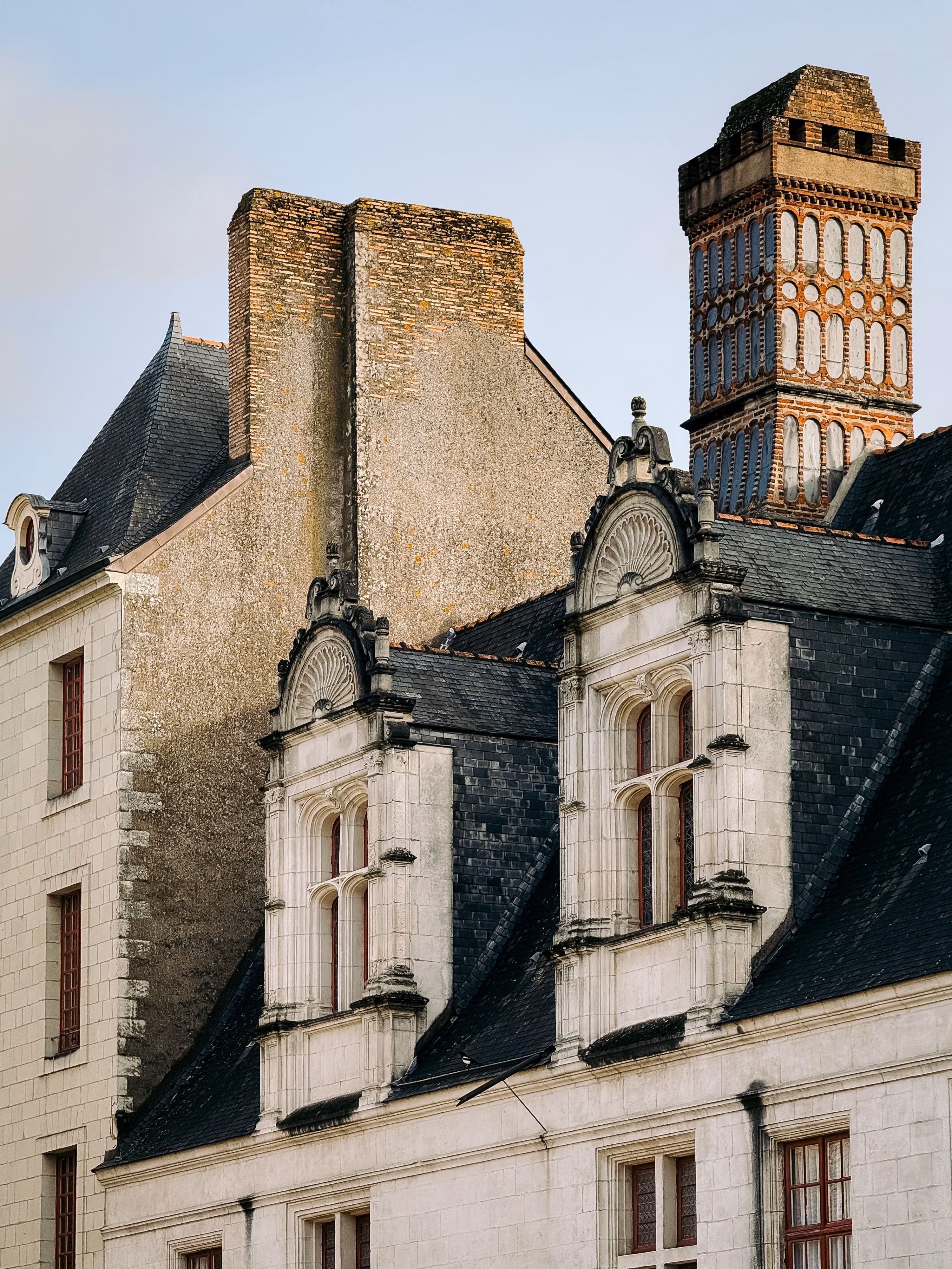 Façade historique avec fenêtres ornées et grandes cheminées en briques sous un ciel clair.