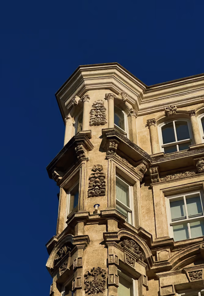 Détail d'un coin d'un bâtiment ancien avec fenêtres, colonnes, et ornements sous un ciel bleu.