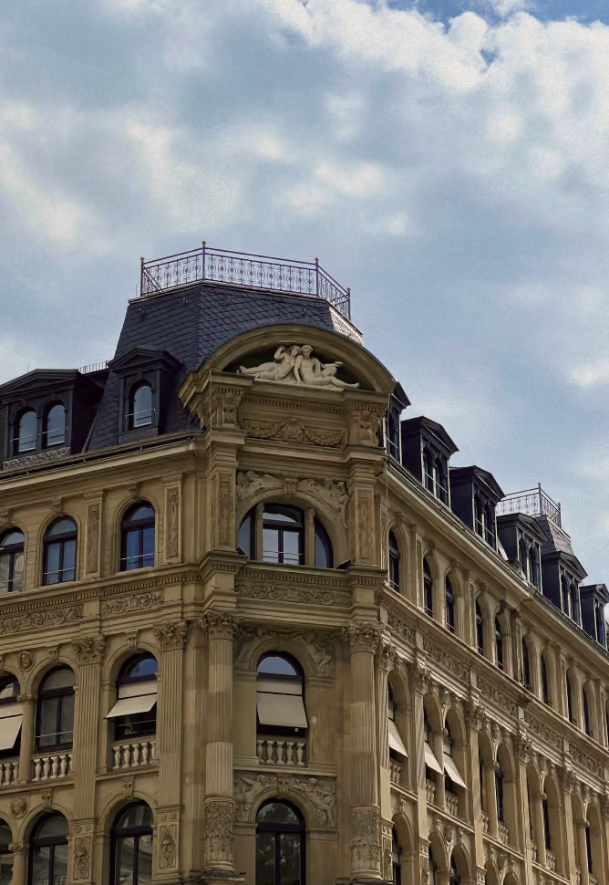 Façade d'un immeuble ancien avec fenêtres à arcades et décorations sculptées sous un ciel nuageux.