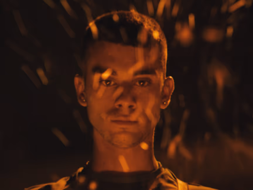 cinco main image, the main character looks at a fire with sparkles in his face.