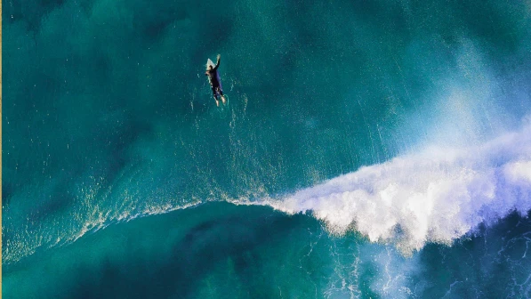A surfer skillfully rides a large wave in the ocean, showcasing their balance and agility against the blue water backdrop.