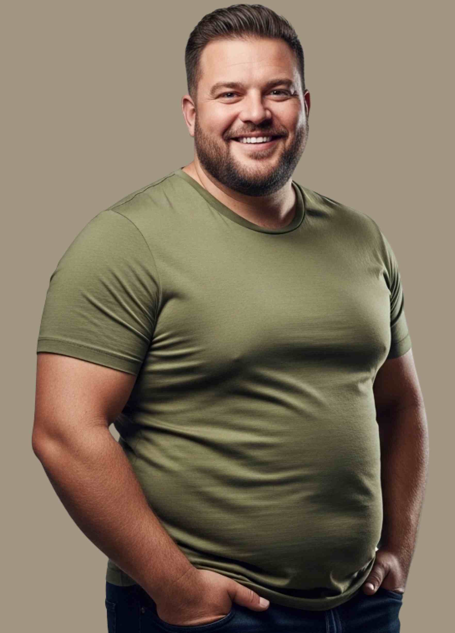 Smiling man with short dark hair and beard wearing an olive green t-shirt standing with hands in pockets against a plain background.