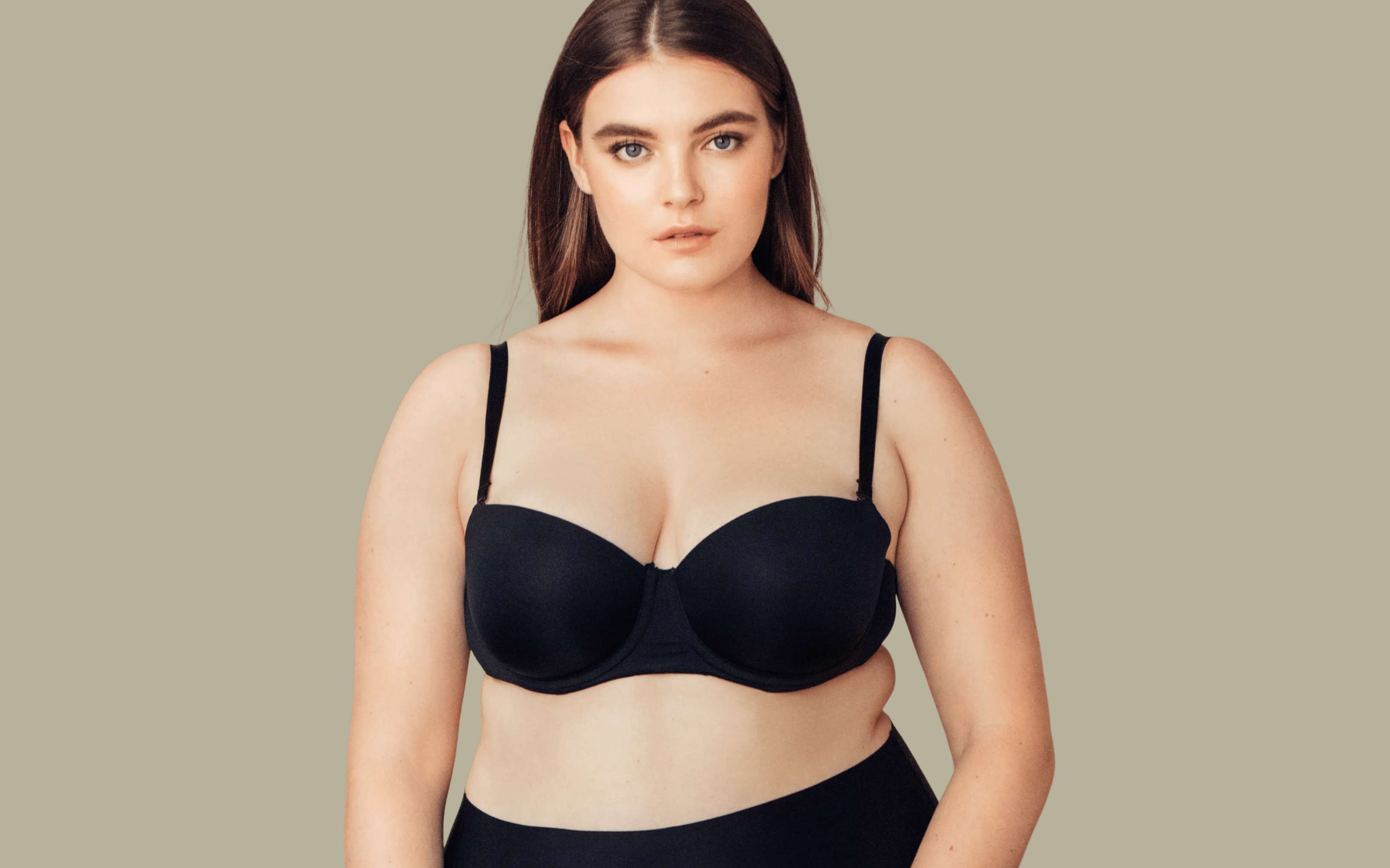 Young woman wearing a black bra and black bottoms against a plain beige background.