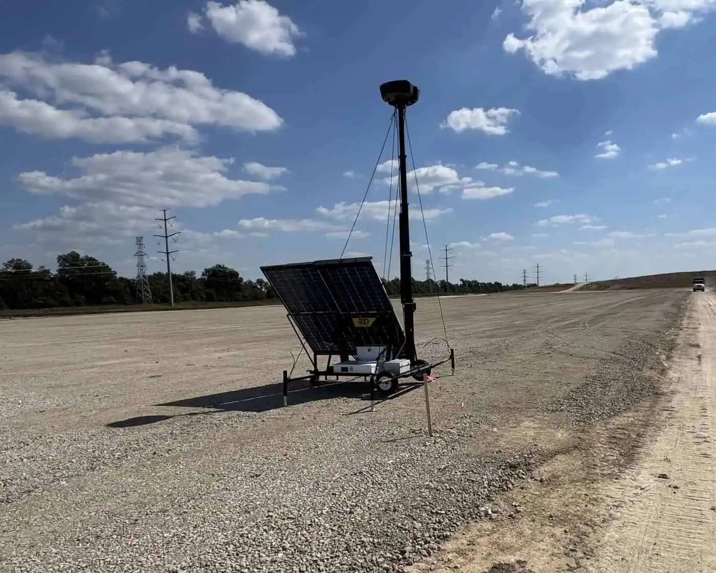 RIO Edge AI mobile security trailer on a construction site access road with its mast raised and solar array deployed