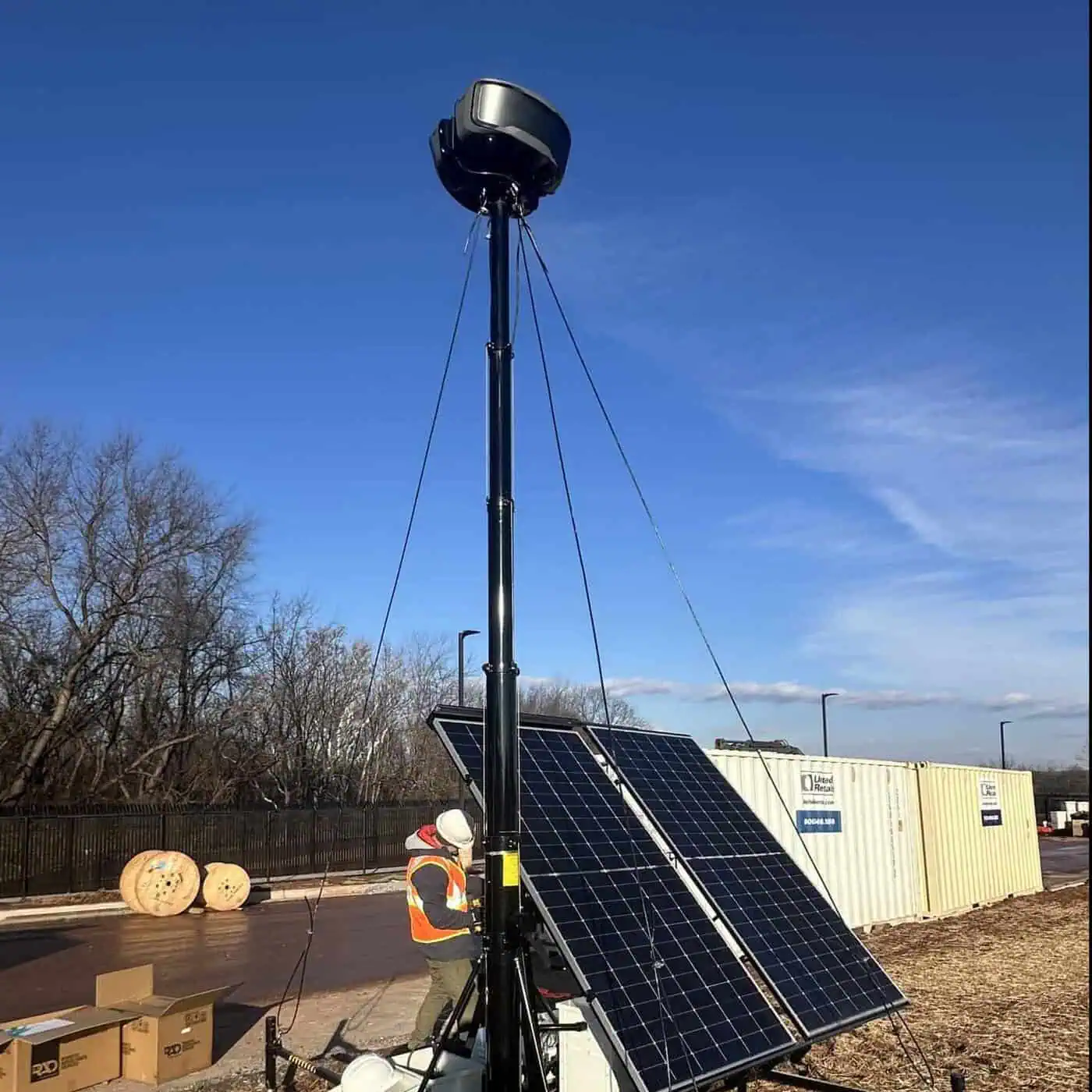 Technician installs a RIO Mini solar security trailer beside shipping containers at a construction site