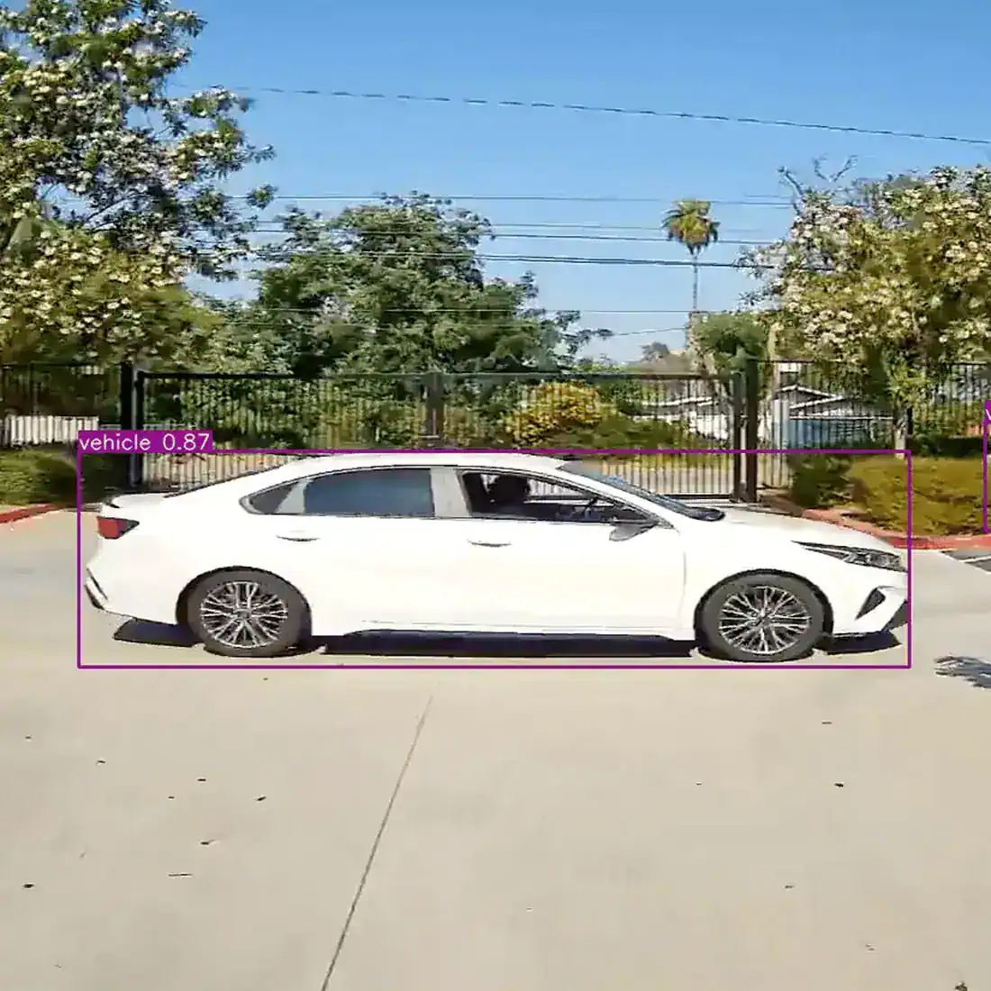 White sedan passing a gated entrance, outlined by a detection box labeled vehicle 0.87