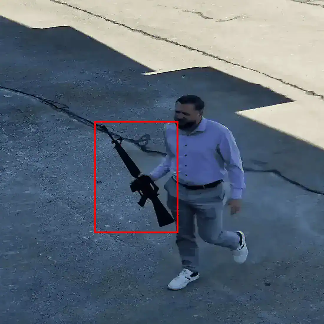 Man carrying a rifle across a parking lot with the firearm outlined in a red detection box