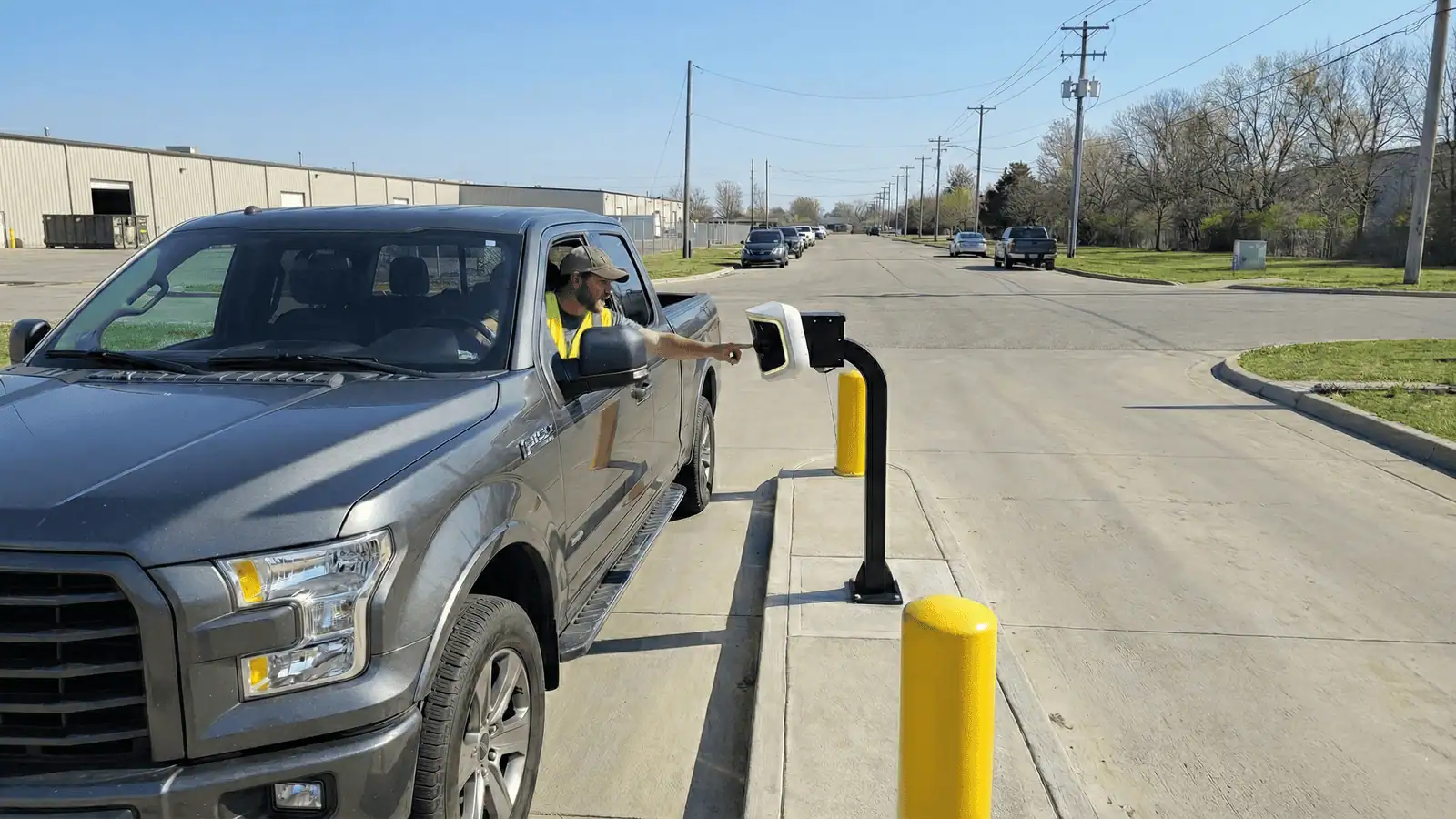 Driver in a high-visibility vest checking in at an AVA Gen4 unit on a curbside pedestal at an industrial park entrance