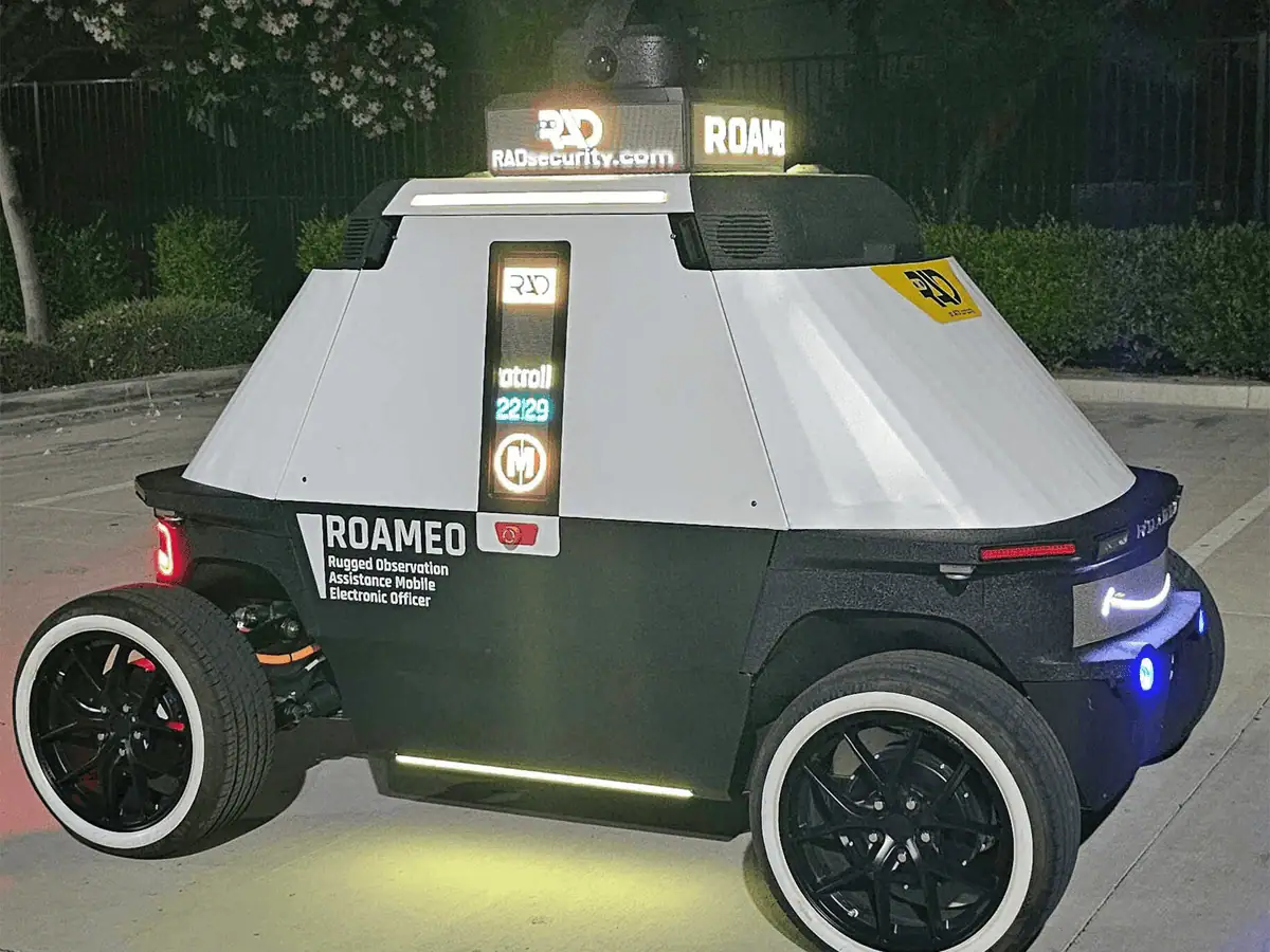 ROAMEO at night with its status display, rear light bar, and wheel lights on beside a hedge