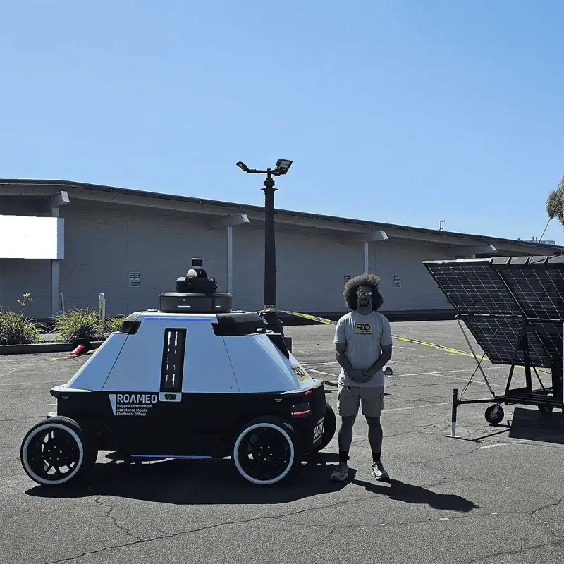 ROAMEO parked beside a RIO solar security trailer and a RAD team member in a sunny lot