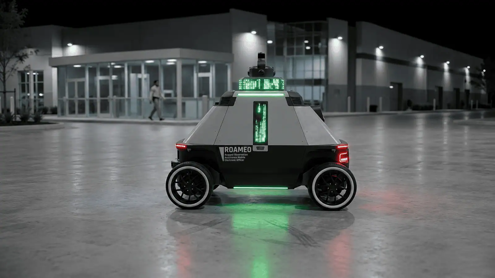 ROAMEO with its LED signage lit on patrol outside an industrial building at night as a person walks past
