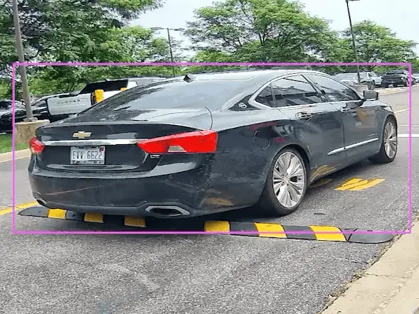 Gate camera view of a sedan at a speed bump with a detection box around the car and its rear plate