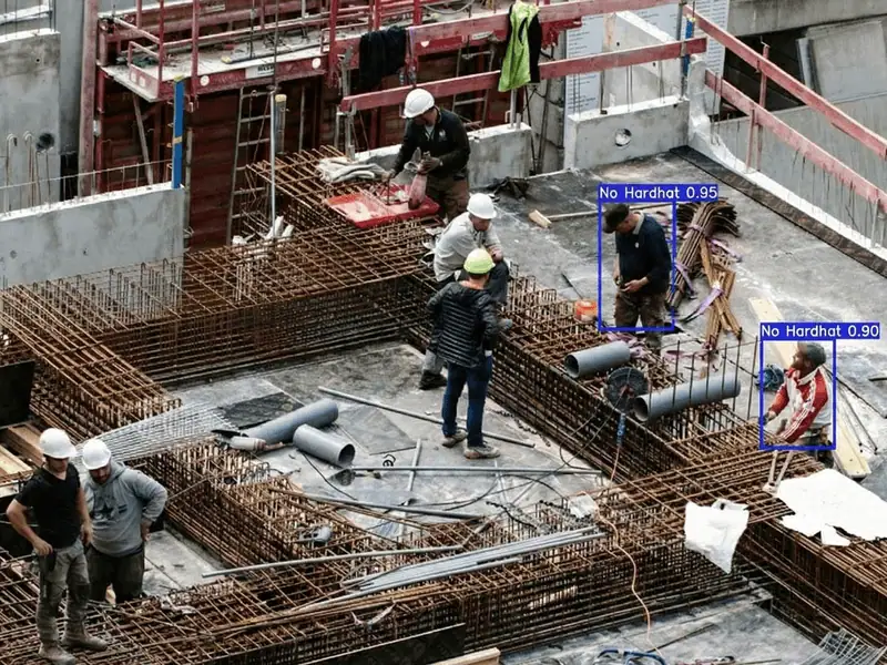 Construction site camera view with detection boxes flagging two workers with no hard hat