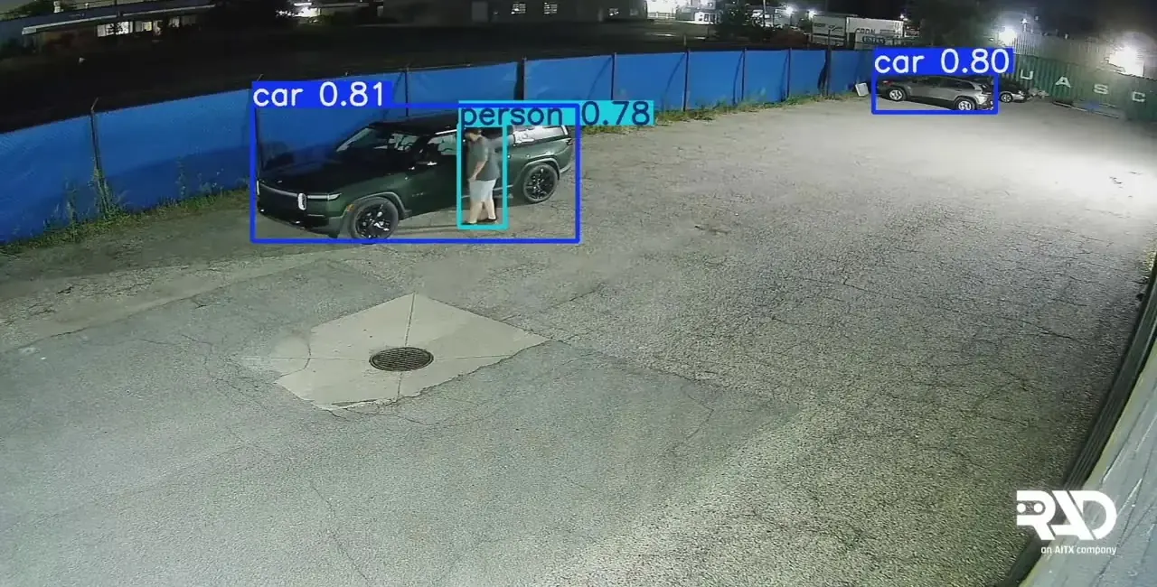 Night camera view of an employee lot: a person at a parked SUV after hours, with car and person detection boxes