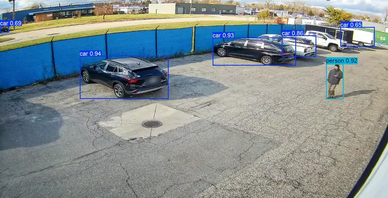 Real RAD camera frame of an employee parking lot, a person inside a cyan person detection box and parked cars in blue boxes