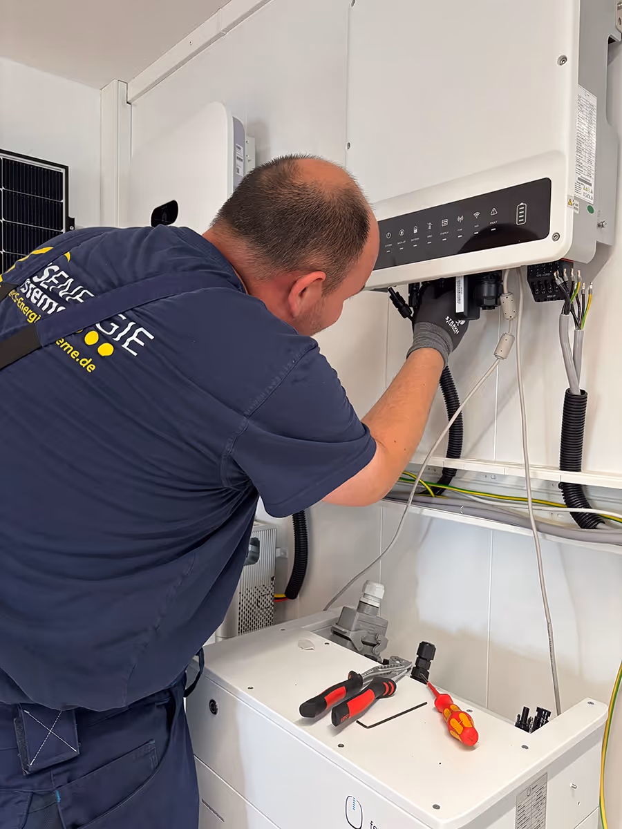 Techniker installiert oder wartet eine weiße elektrische Anlage an einer Wand, mit Werkzeugen auf einem weißen Gerät in der Nähe.