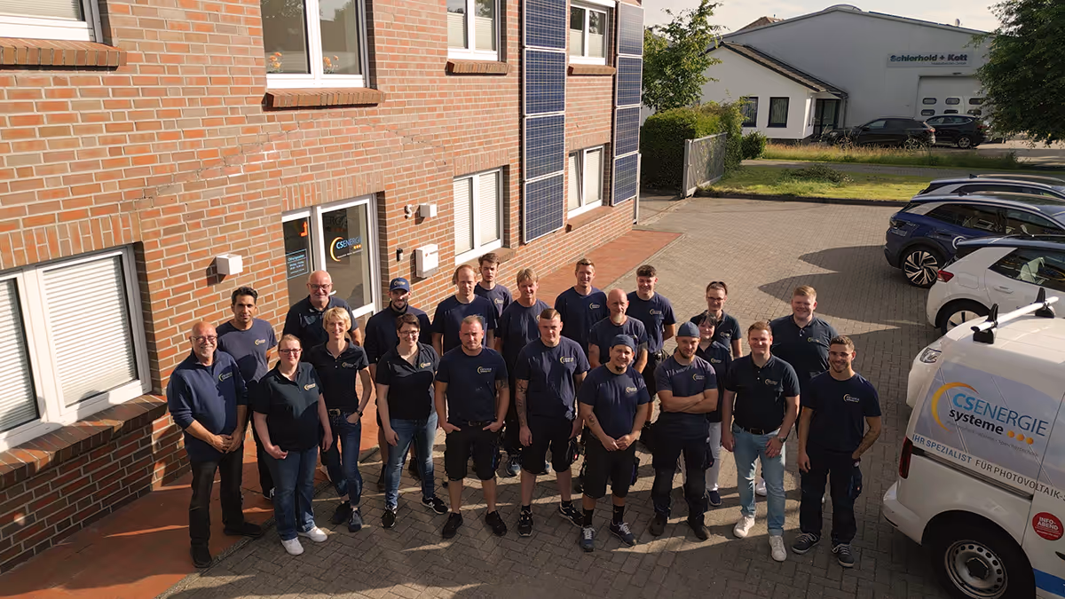 Gruppenfoto von 21 Personen in Firmenkleidung vor einem Backsteingebäude mit Solarpanelen und einem weißen Fahrzeug mit CS Energie Systeme Logo.