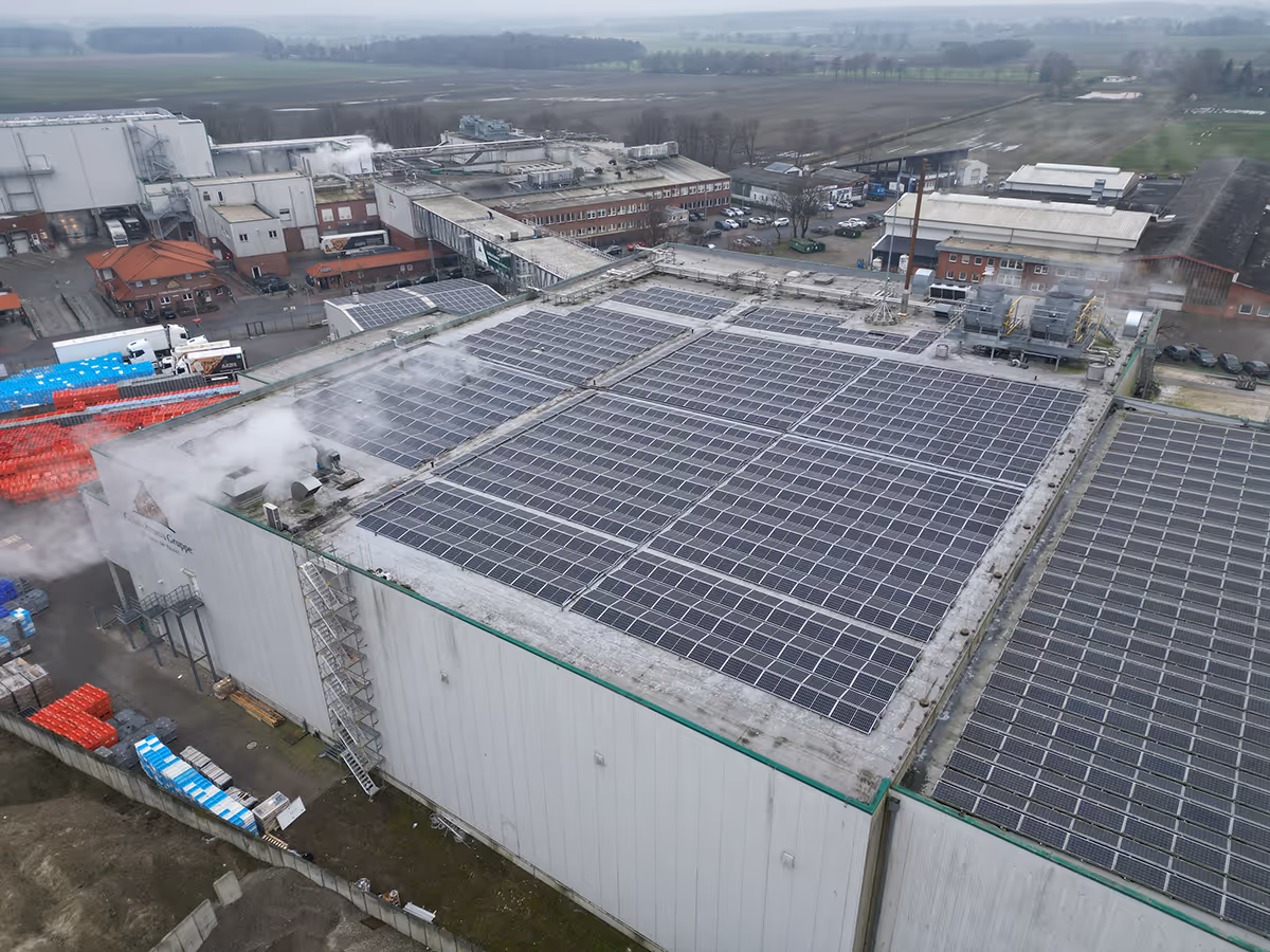 Luftaufnahme eines Industriegebäudes mit vielen Solarpaneelen auf dem Dach und Dampf, der aus Abluftanlagen austritt.