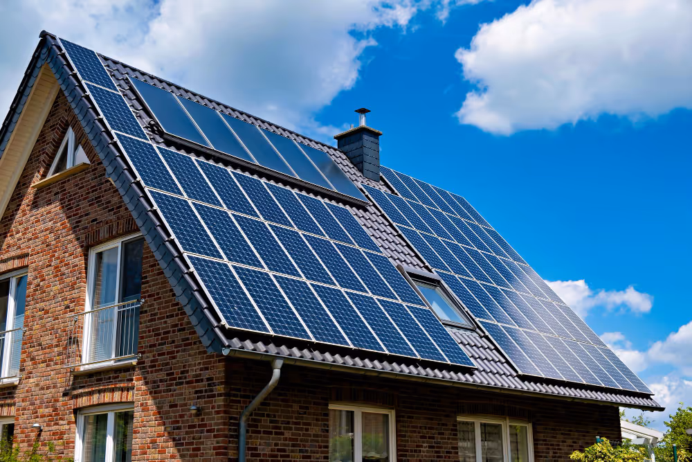 Hausdach mit mehreren installierten Solarmodulen unter blauem Himmel mit Wolken.