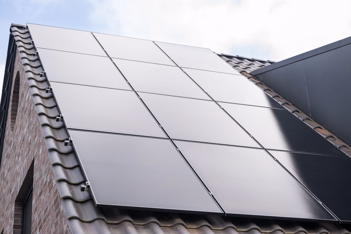 Dach eines Hauses mit installiertem Solarpanel-Array aus zwölf schwarzen Paneelen auf Ziegelziegel-Dach.