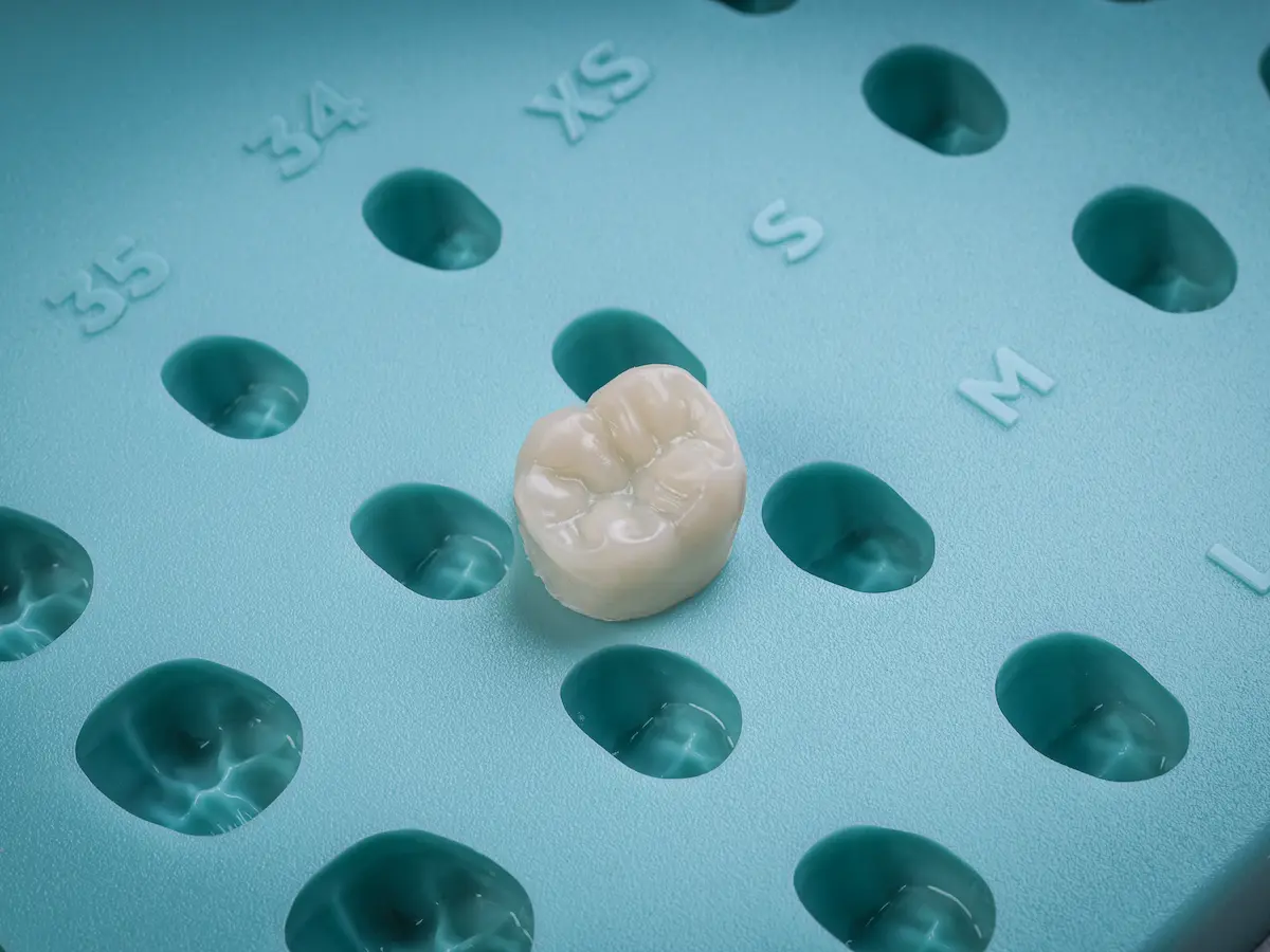 A single dental crown placed on a blue mold tray with numbered and lettered slots for different crown sizes.