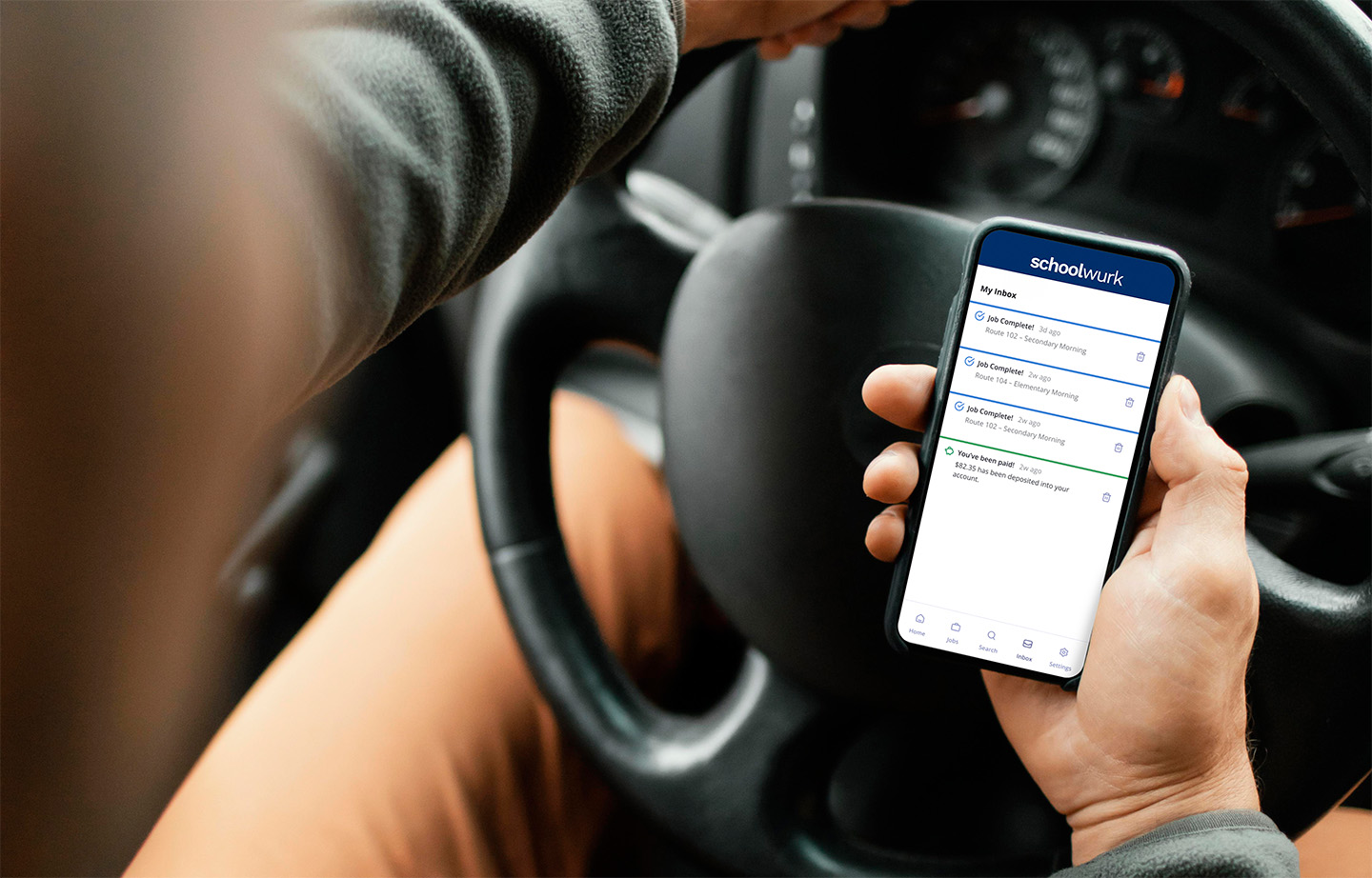 Bus driver holding a phone with Schoolwurk notifications on the screen