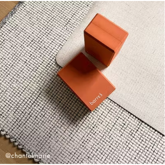 Mujer con cabello rizado con ropa deportiva de color óxido realizando una sentadilla con una banda de resistencia alrededor de sus muslos.