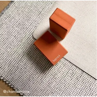 Mujer con cabello rizado con ropa deportiva de color óxido realizando una sentadilla con una banda de resistencia alrededor de sus muslos.