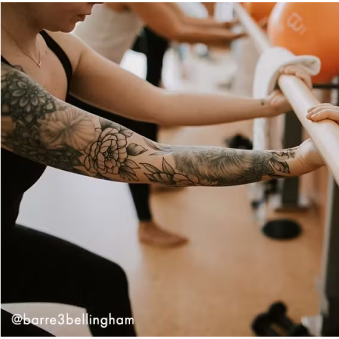 Mujer con cabello rizado con ropa deportiva de color óxido realizando una sentadilla con una banda de resistencia alrededor de sus muslos.
