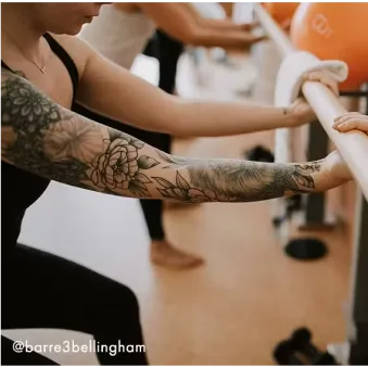 Mujer con cabello rizado con ropa deportiva de color óxido realizando una sentadilla con una banda de resistencia alrededor de sus muslos.