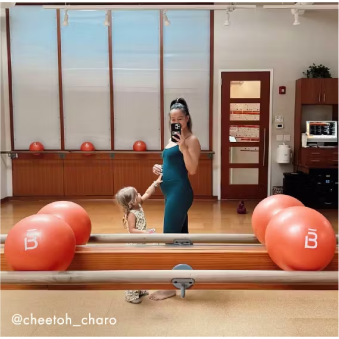 Mujer con cabello rizado con ropa deportiva de color óxido realizando una sentadilla con una banda de resistencia alrededor de sus muslos.