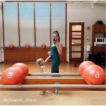 Mujer con cabello rizado con ropa deportiva de color óxido realizando una sentadilla con una banda de resistencia alrededor de sus muslos.