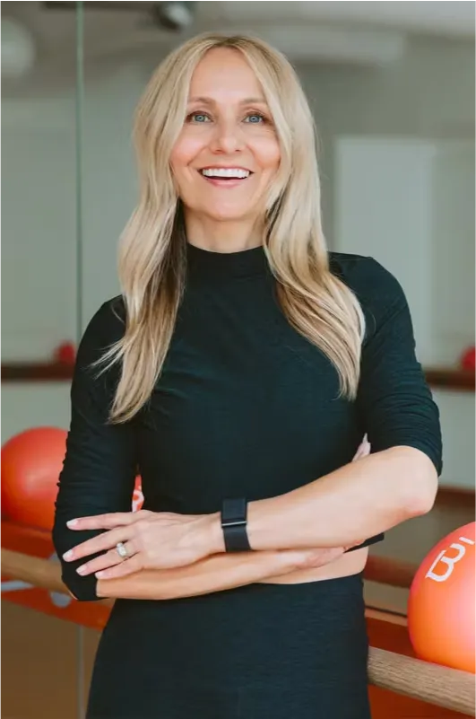 Sadie Lincoln, vestida con una camiseta negra de manga larga y un rastreador de actividad física, de pie con los brazos cruzados en un gimnasio de barre3.