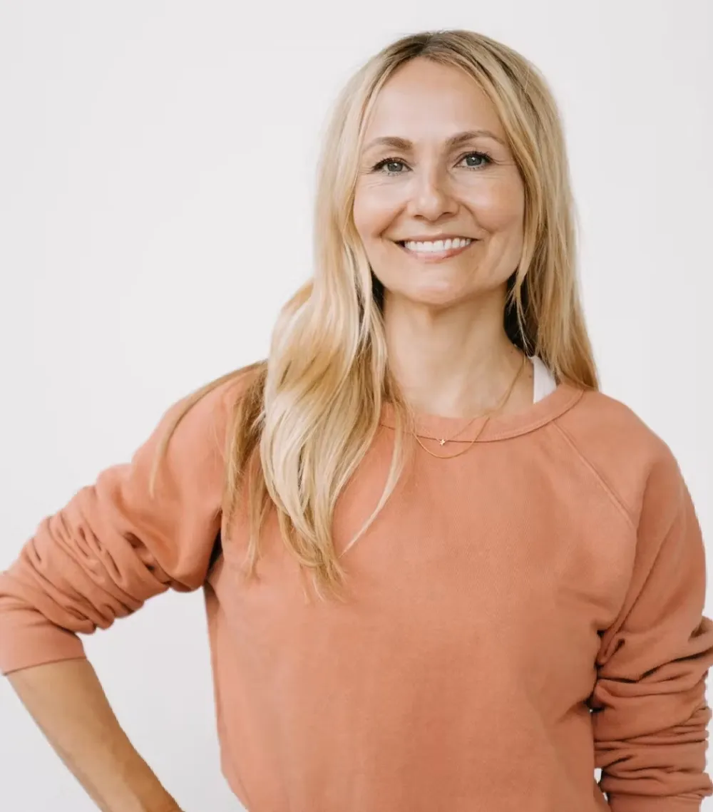 Sadie Lincoln, vestida con una sudadera naranja claro y de pie frente a un fondo blanco liso.