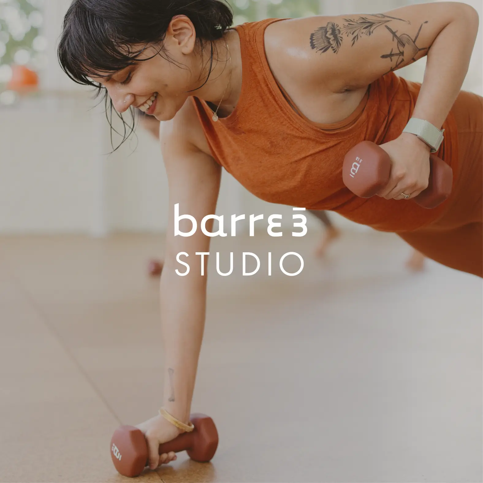 Mujer sonriente en un traje deportivo naranja sosteniendo mancuernas en posición de plancha en un estudio de fitness barre3 Santiago.