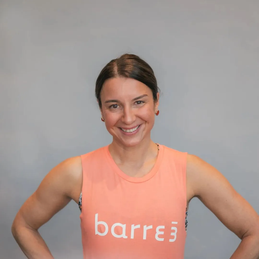 Claudia Dienemann con una blusa sin mangas de color coral con la palabra 'barre3' de pie sobre un fondo gris.