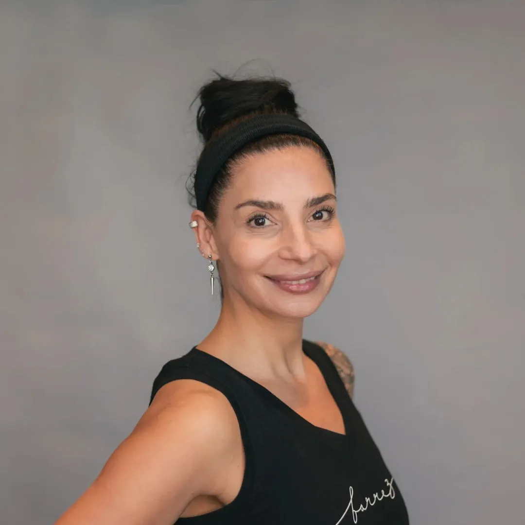 Romina Rodríguez con una camiseta negra sin mangas, posando sobre un fondo gris en barre3 Santiago.