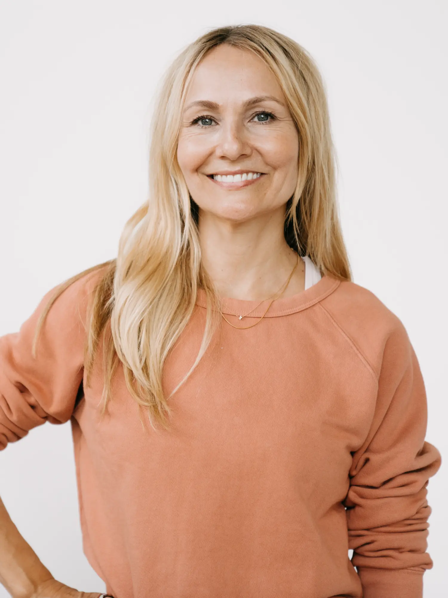 Sadie Lincoln fundadora de barre3 sonriendo con una sudadera coral sobre un fondo blanco.