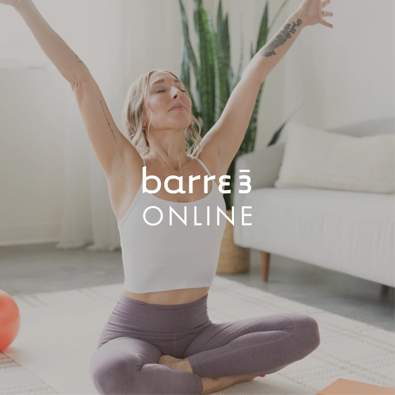 Mujer en pose de yoga sentada con las piernas cruzadas sobre una colchoneta y los brazos levantados, el texto superpuesto dice 'barre3 ONLINE'.