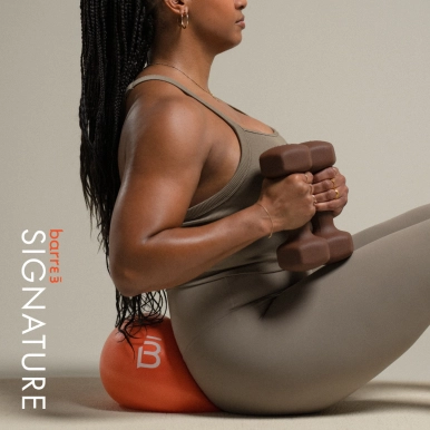 Mujer en forma con ropa deportiva gris sosteniendo mancuernas marrones, sentada sobre un cojín naranja con el texto característico de barre3 Santiago.