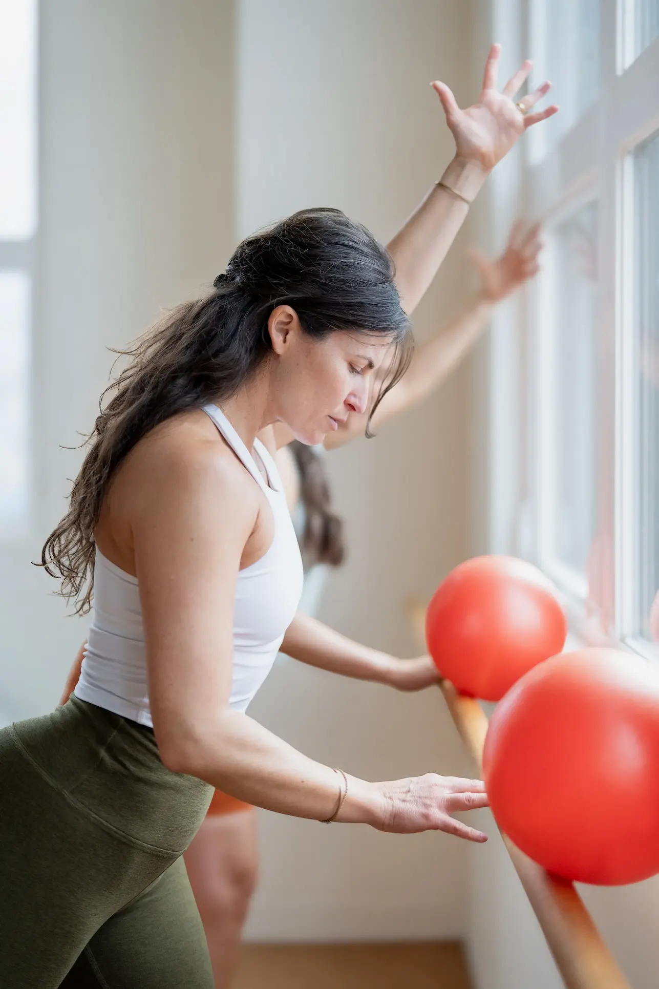 Mujeres vestidas con ropa deportiva realizando un ejercicio de levantamiento de piernas de pie con bandas de resistencia en un luminoso estudio de fitness barre3 Santiago.