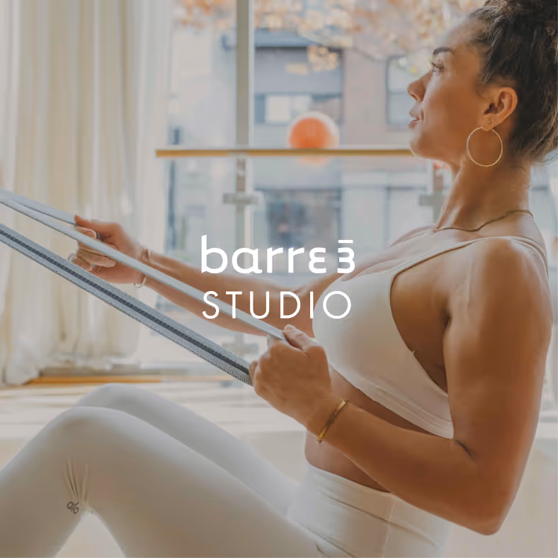 Mujer sonriente en un traje deportivo naranja sosteniendo mancuernas en posición de plancha en un estudio de fitness barre3 Santiago.