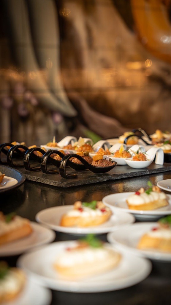 Two plates of pasta with grilled vegetables, cherry tomatoes, basil, a slice of lemon, and a round piece of mozzarella topped with pesto and pine nuts.