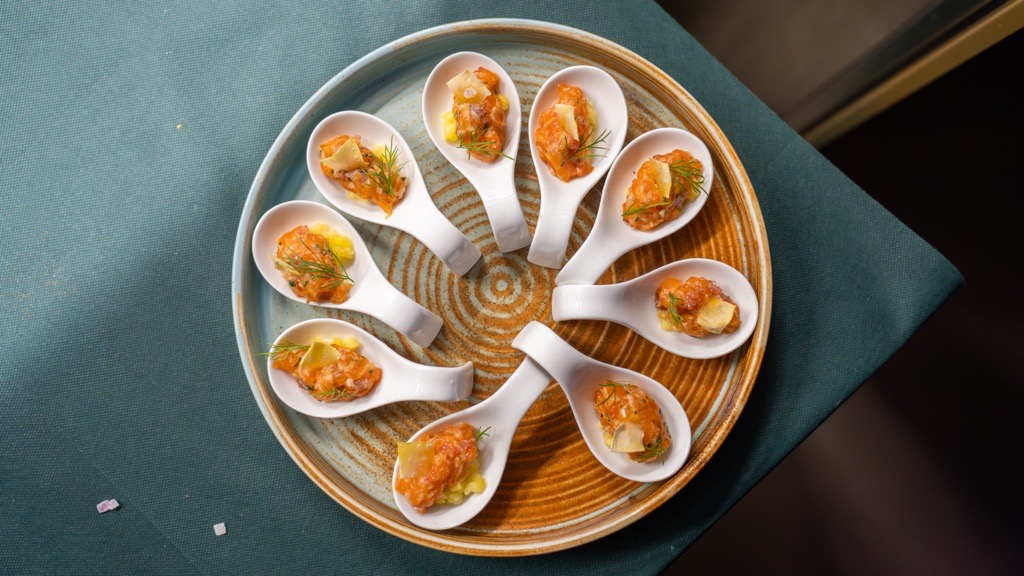 Plate of sliced medium-rare steak served over tagliatelle pasta with tomato sauce and a side of mixed green salad.