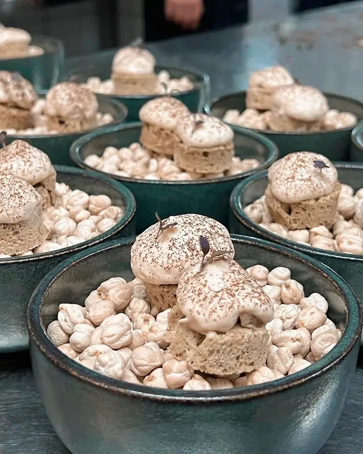 Multiple bowls filled with dried chickpeas topped with two small pieces of bread and dollops of cream sprinkled with cocoa powder.