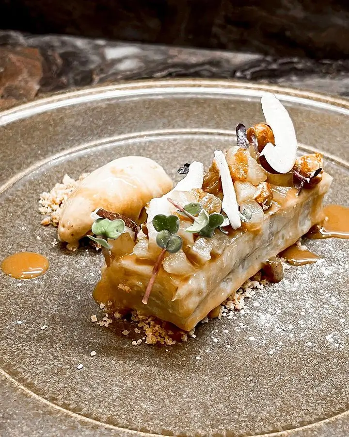 Gourmet dessert with caramel sauce, microgreens, and coconut flakes on a textured plate.