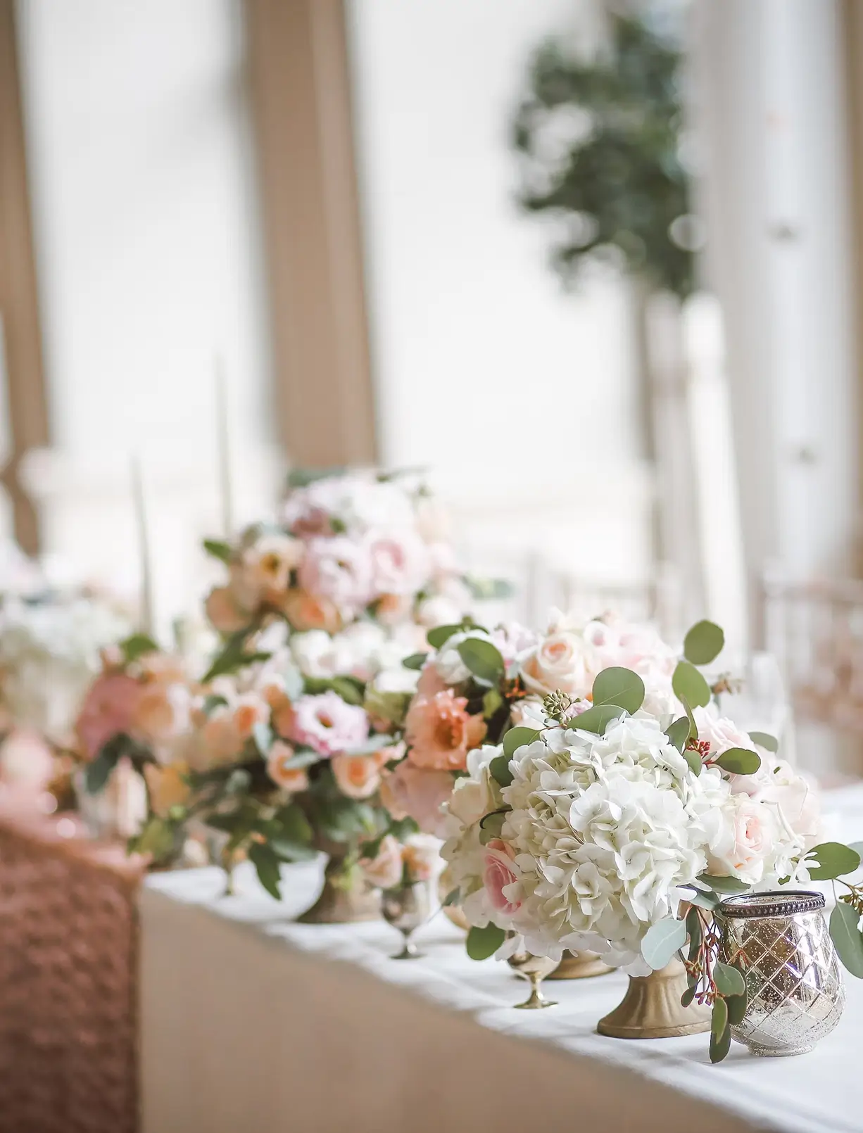 Elegant table arrangement with bouquets of white and pink flowers and a decorative glass candle holder.
