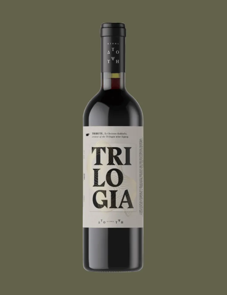 Bottle of red wine labeled 'Trilogia' on a muted olive background.