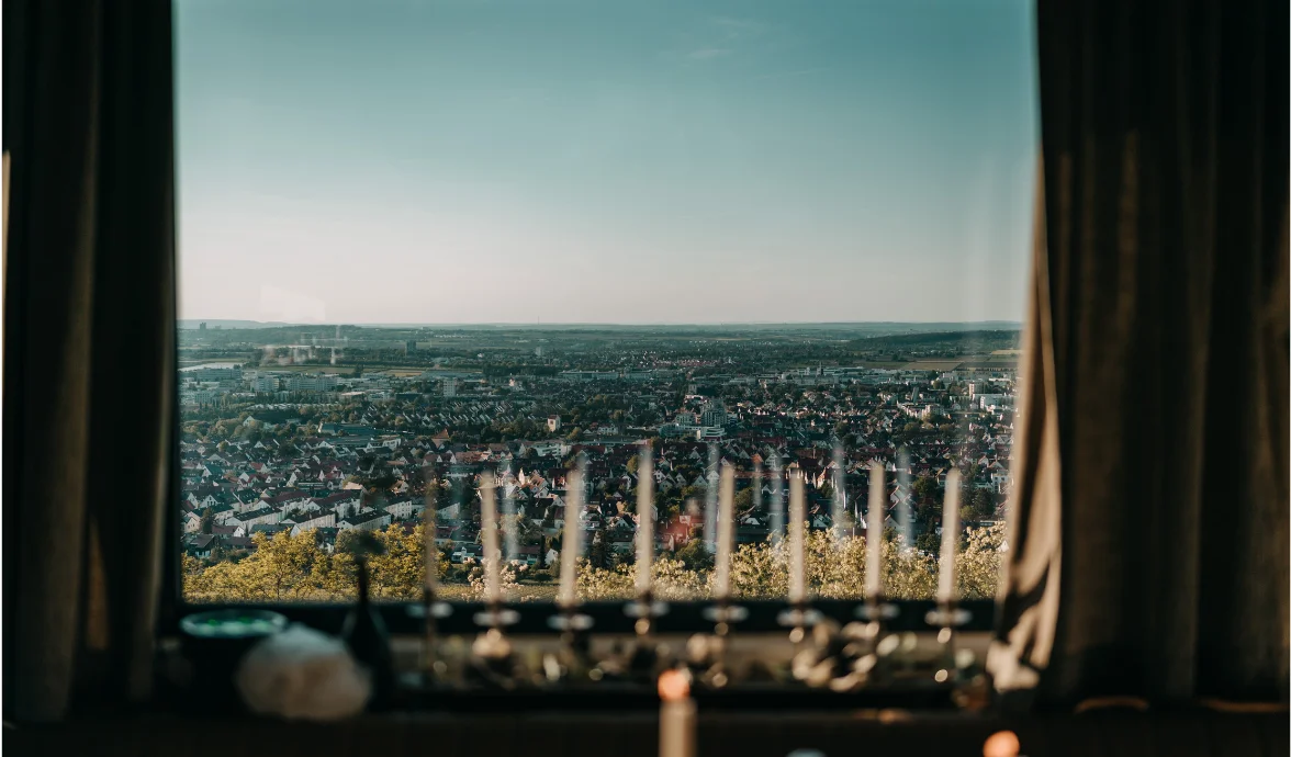 Cityscape view through a window with blurred candles and curtains in the foreground.