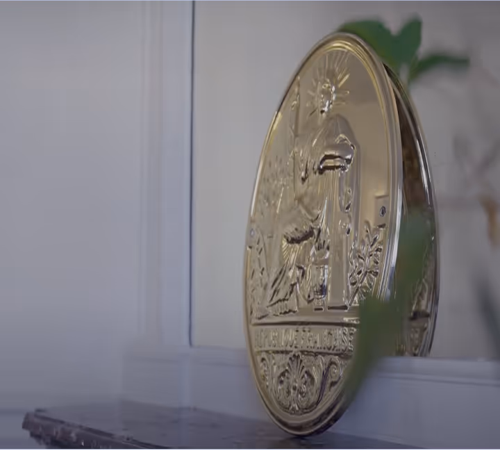 Un grand médaillon doré avec des gravures détaillées affiché sur une étagère contre un mur blanc.